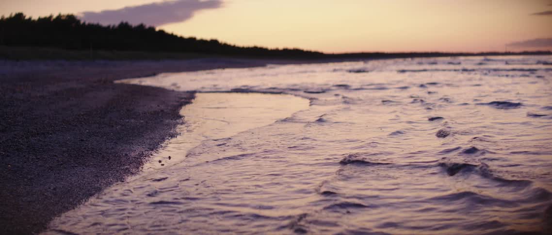 The tide gently washing into a beach at sunset