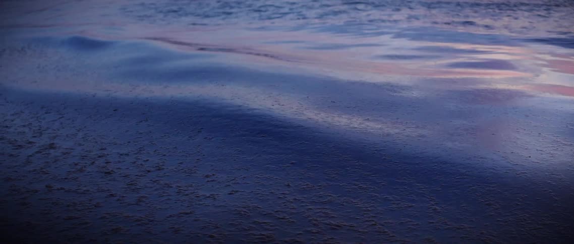 Gentle waves glide along the surface of the ocean water under minimal daylight