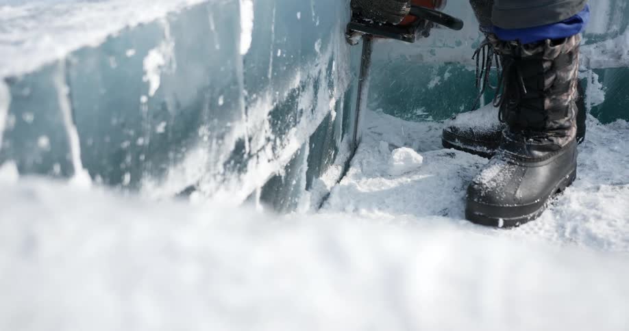 A person carves a very thick block of ice with a chainsaw