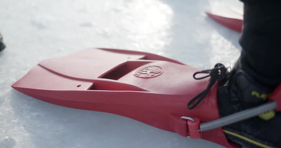 A person with a type of flipper strapped to their boot walks across ice