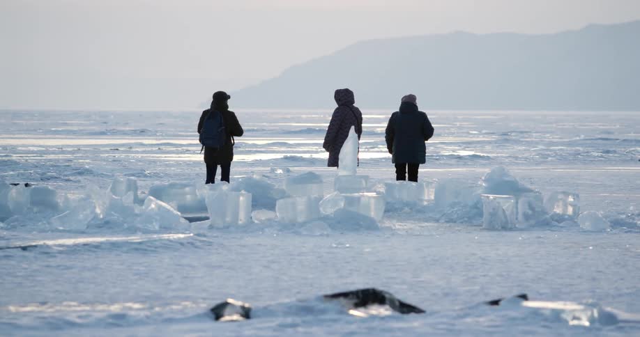 Three people are walking across a snow and ice covered flat area