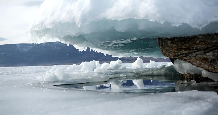 Large ice cap hanging over a rock melting into a puddle in the ocean below