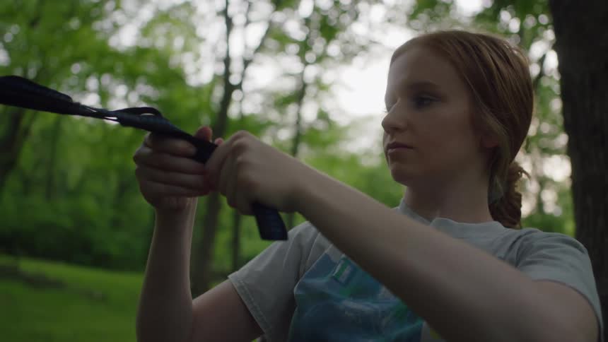 A girl is attaching a rope to the tree in the forest