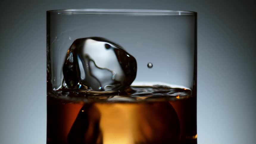 Liquor being poured over ice cubes in a glass