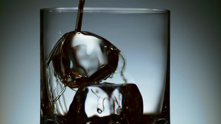 Liquor being poured over ice inside a glass