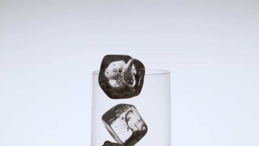 Five ice cubes are dropped into a glass in a studio