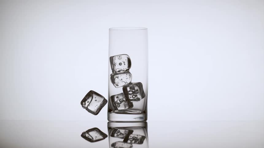 The ice cube bounces off the glass onto the table