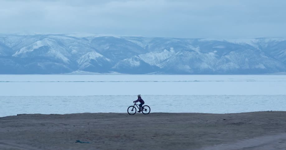 Person rides a bicycle near a lake close to the snow covered mountains