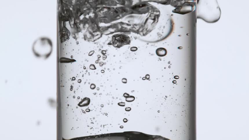 One ice cube is dropped into a glass of mineral water