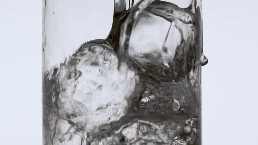 Soda is poured into a glass with ice cubes