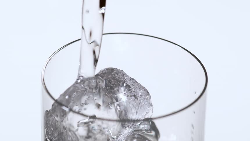 Water being poured in to a glass with ice cubes