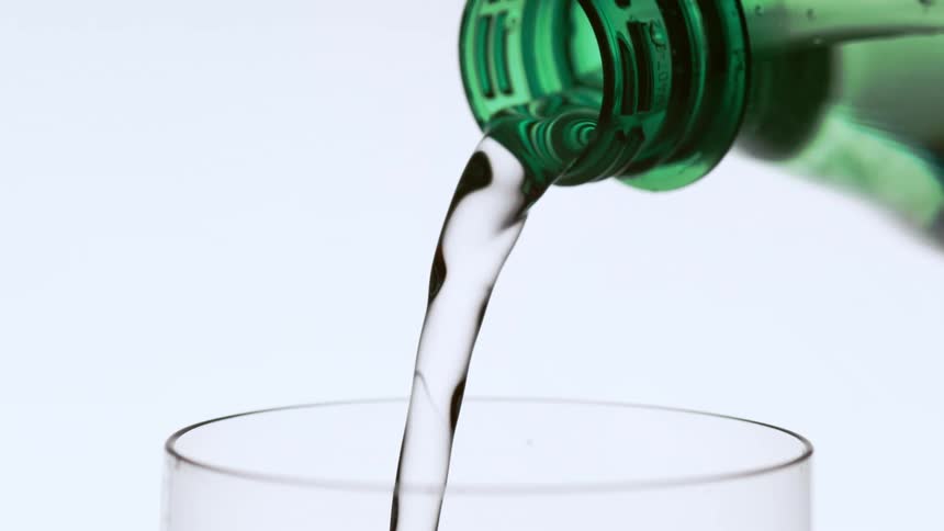 Water pours from a green bottle in a drinking glass