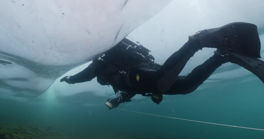 Scuba diver swims under the ice in the green ocean water