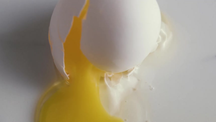 Broken egg spills yolk an white onto flat pale surface