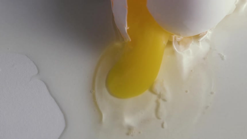 Broken yolk flows out of cracked egg onto white hard surface