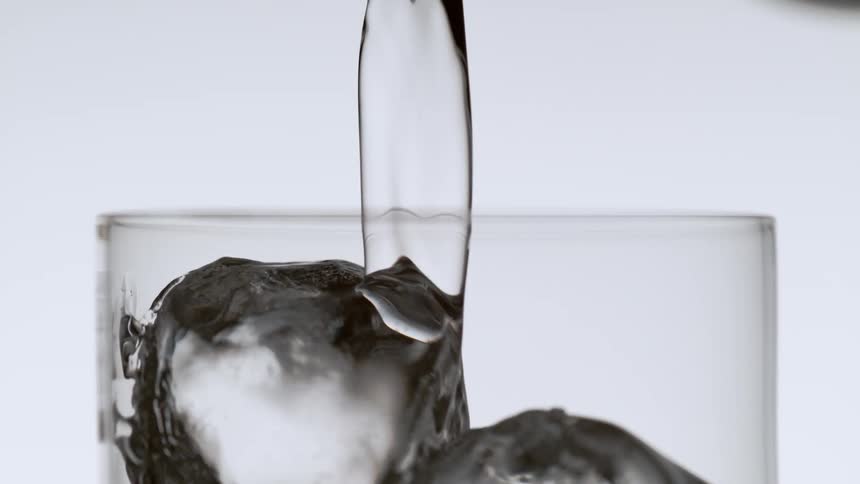 Soda is being poured into a glass with ice cubes