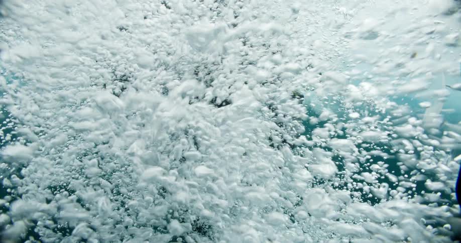 Scuba diver jumps into water under ice creating bubbles