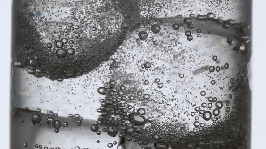 Fizzy mineral water is being poured into a glass with ice cubes