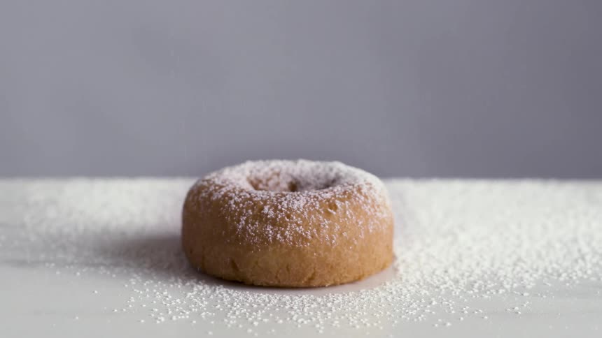 Doughnut over a table being sprinkled with confectioners sugar