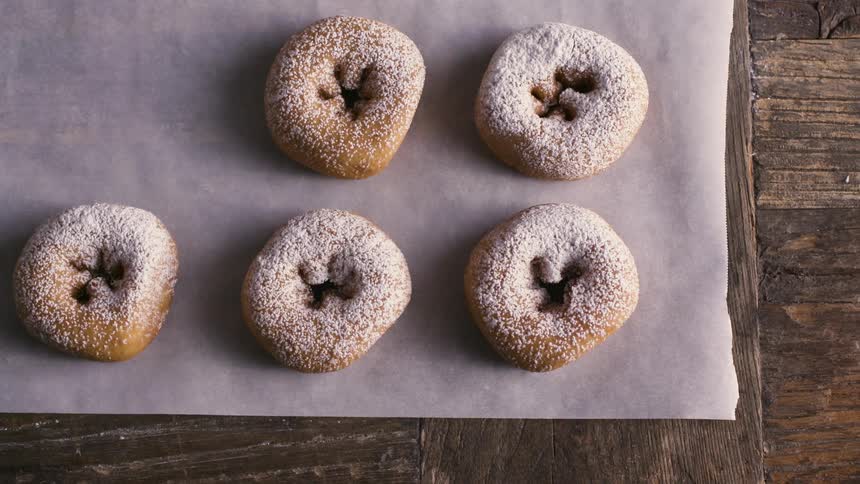 Woman placing doughnuts on cooking paper over a wooden table