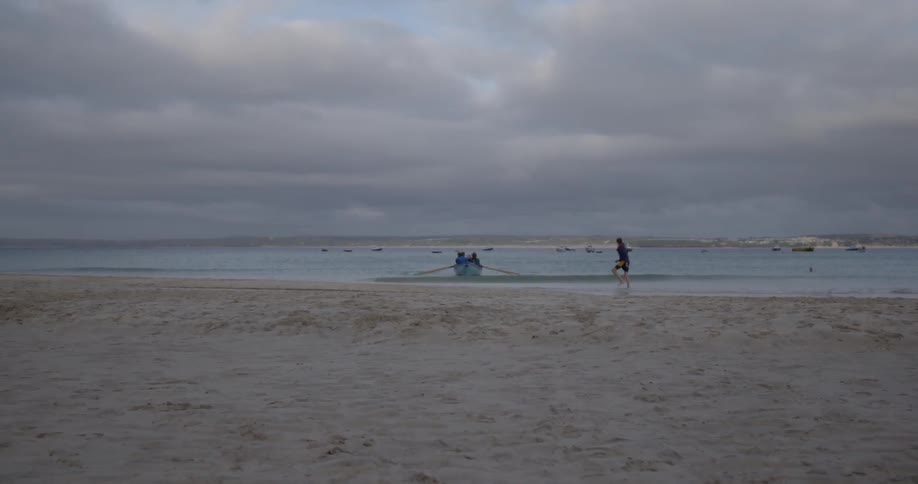 A canoe containing several people approaches the shore of a beach on a cloudy day