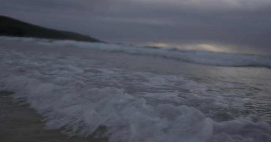 Waves move steadily towards the shore at sunset