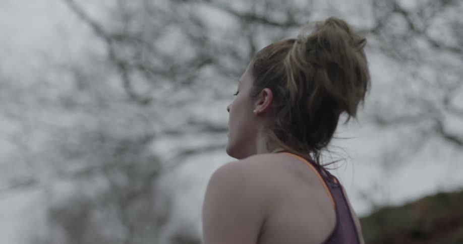 A woman crouches and takes some deep breaths on a cloudy day