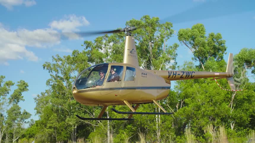 A golden painted helicopter slowly lifts into the air and begins to rotate as it hovers