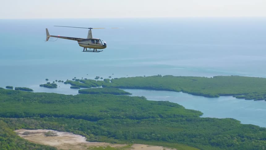 A helicopter flies over a river delta on a sunny day
