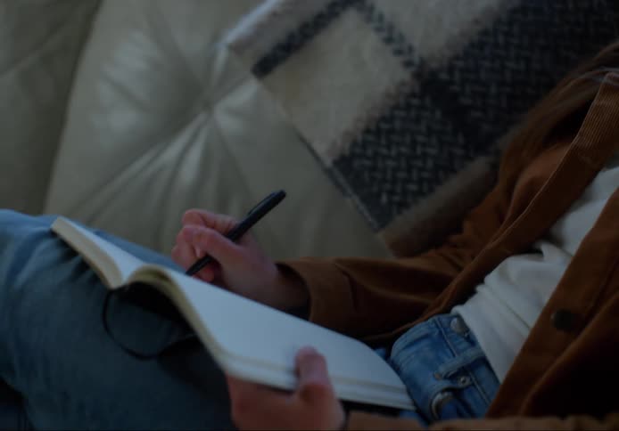 A woman sits on a couch writing in a book