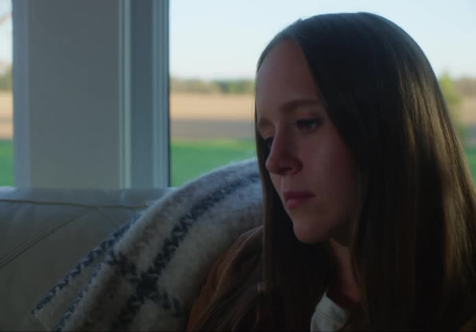 Woman strokes her hair while sitting on a sofa with a blanket