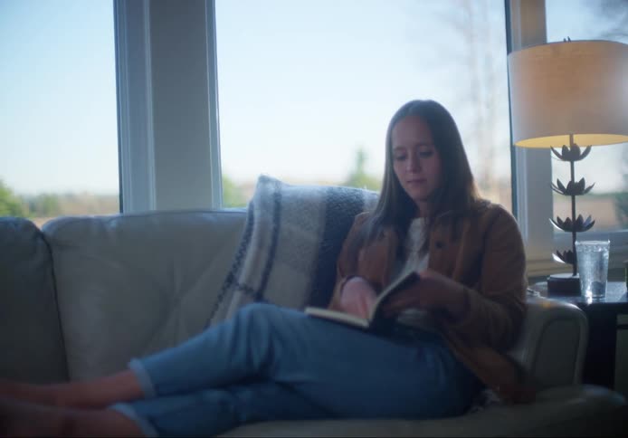 A barefoot woman sits on a sofa and begins writing in a journal