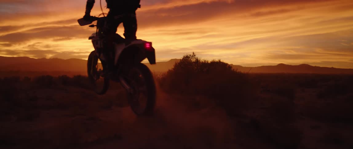 Person drives motocross motorcycle in the desert at sunset