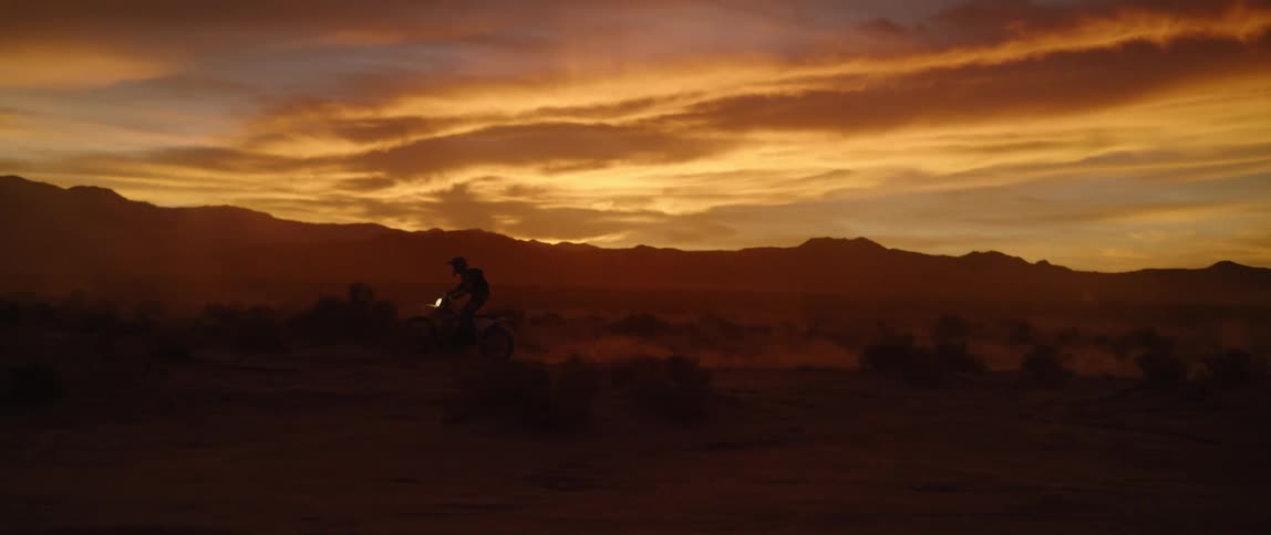 A person rides a dirt bike off road through the badlands at sunset
