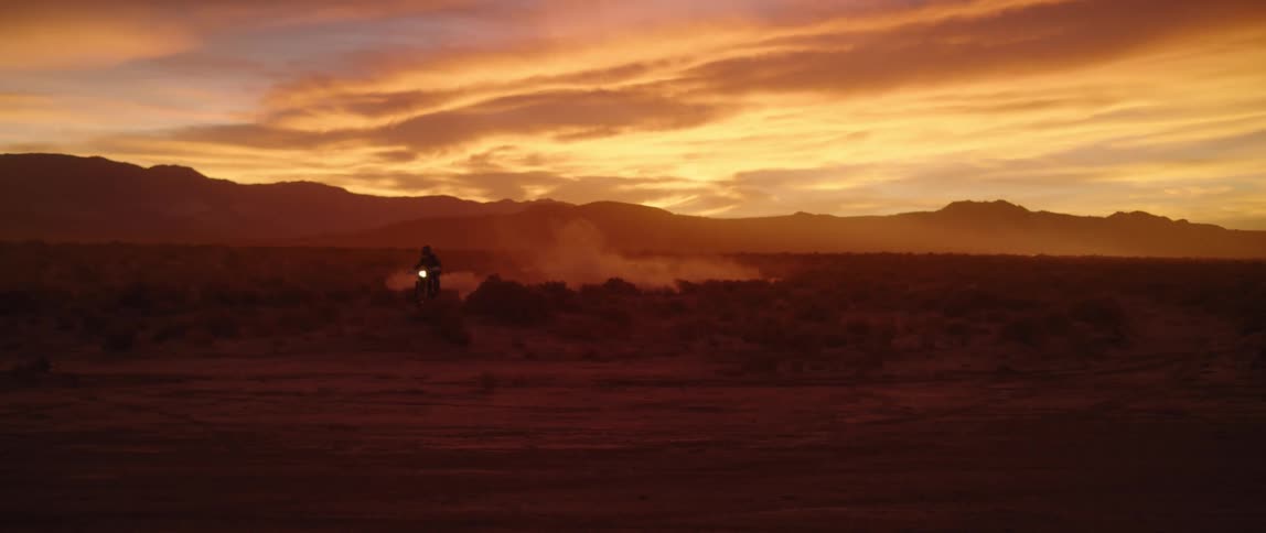 A person rides a motorcycle off road through the desert