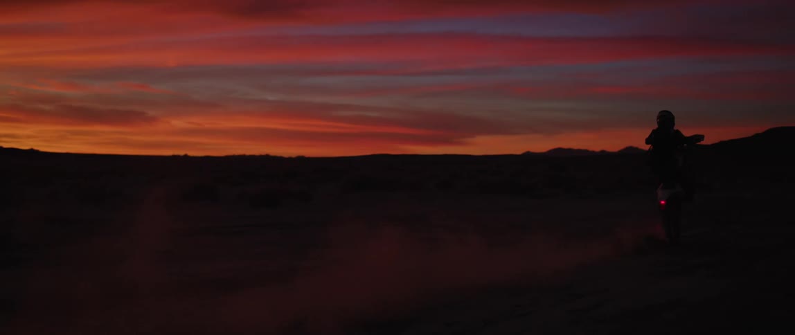 A motorbike rider does a wheelie in the desert near a canyon at sunset