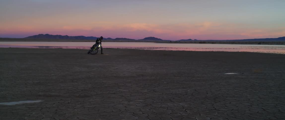 Person doing tight circles riding a motorcycle on the sand near a lake