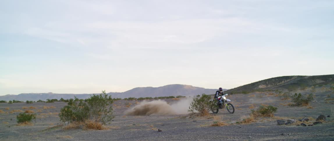 A person rides a dirt bike across the barren rural area