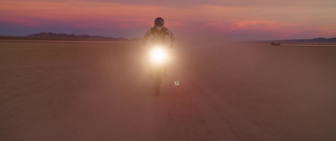 A person on an offroad motorcycle does a wheelie while riding through a desert at sunset