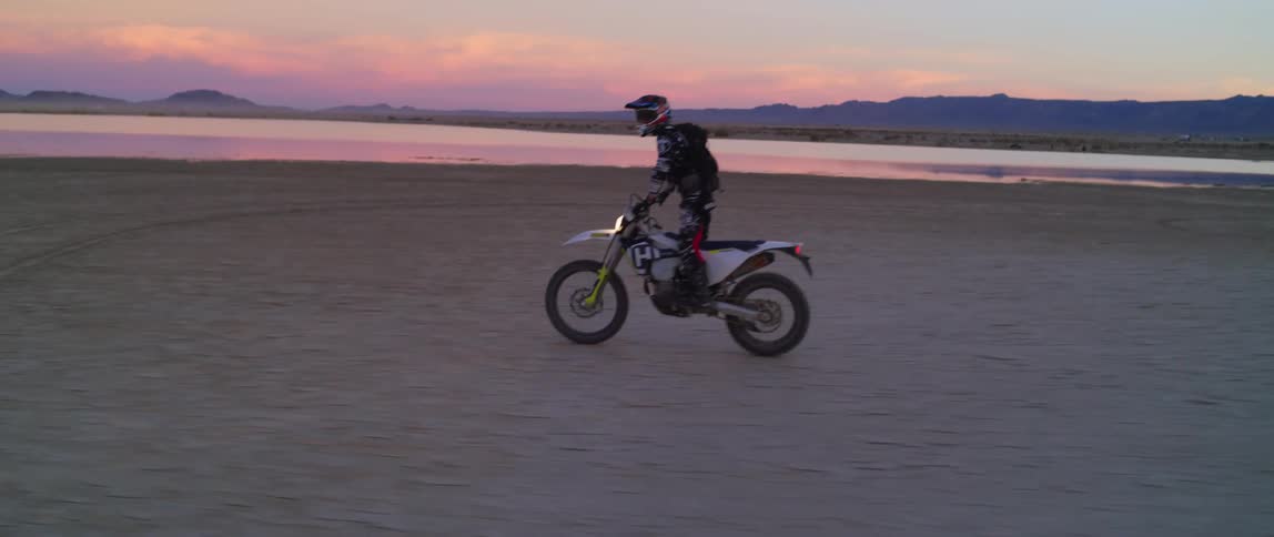 Motorcycle rider stands as he rides the bike on a beach