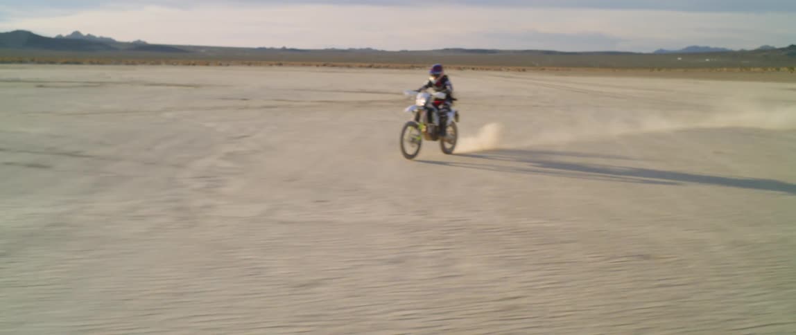 A man rides his dirt bike across a desert