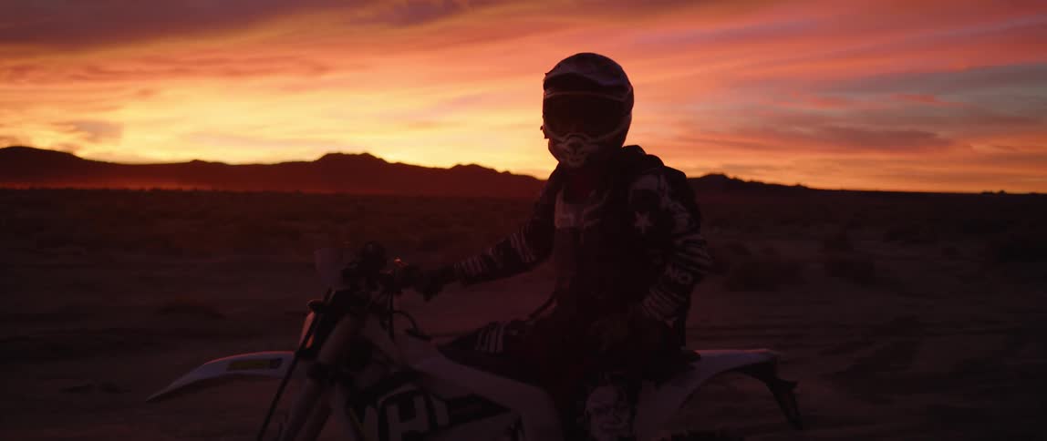 A person sitting on a motorbike with a red sky in the background