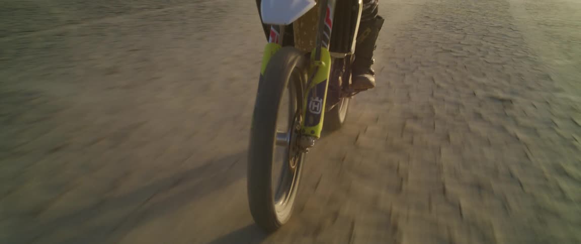 A motorcyclist rides a dirt bike across a field of dry cracked dirt