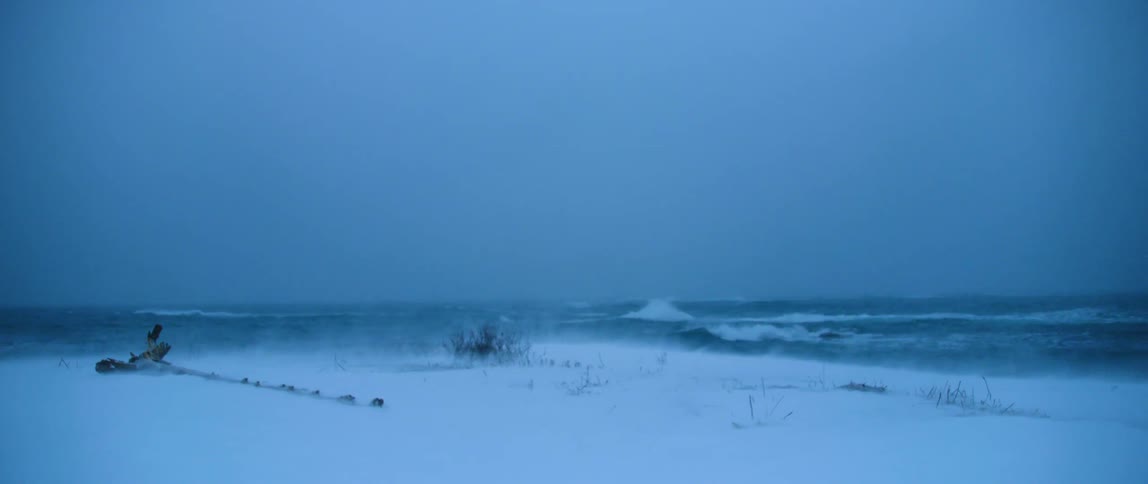 Strong winds blow snow along a coastline battered by white capped seas