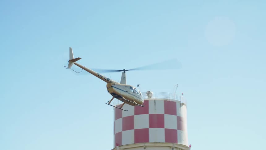 A helicopter flying in the sky with trees and buildings and clouds in the background