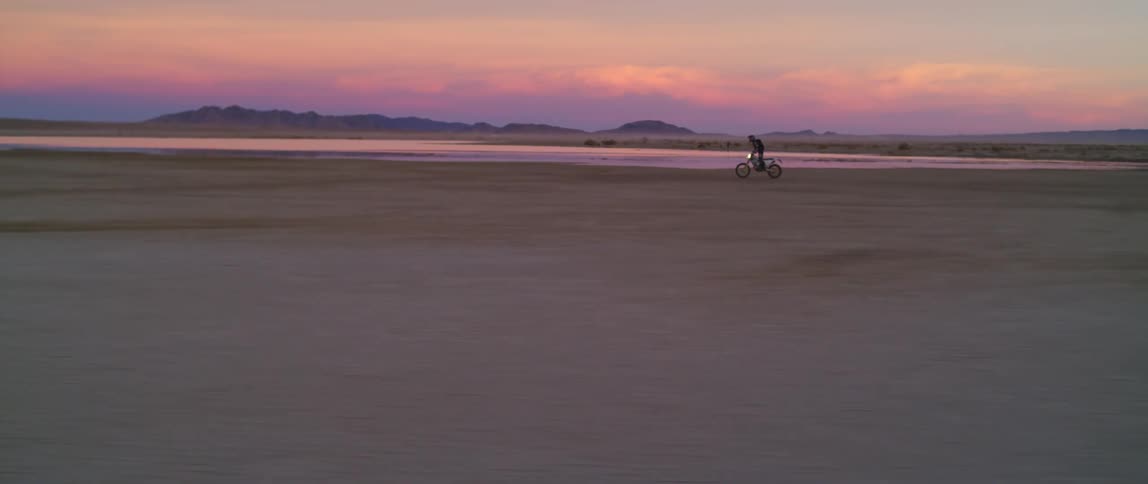 A person rides a motorbike through the desert at sunset