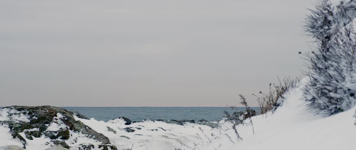 The sun sets on a calm sea lined with a snow covered coast