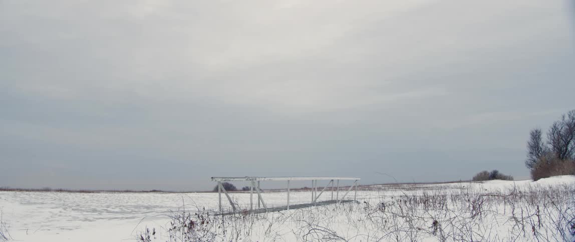 A foot ramp pulled from the nearby water sits in a snow covered field on a cloudy day