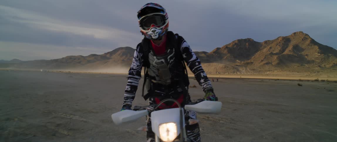A motocross rider stands up as he rides through the desert near a canyon