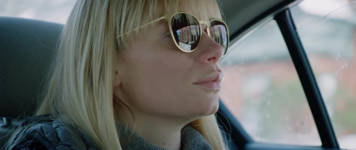 A blonde haired woman looks out the rear passenger window of a taxi